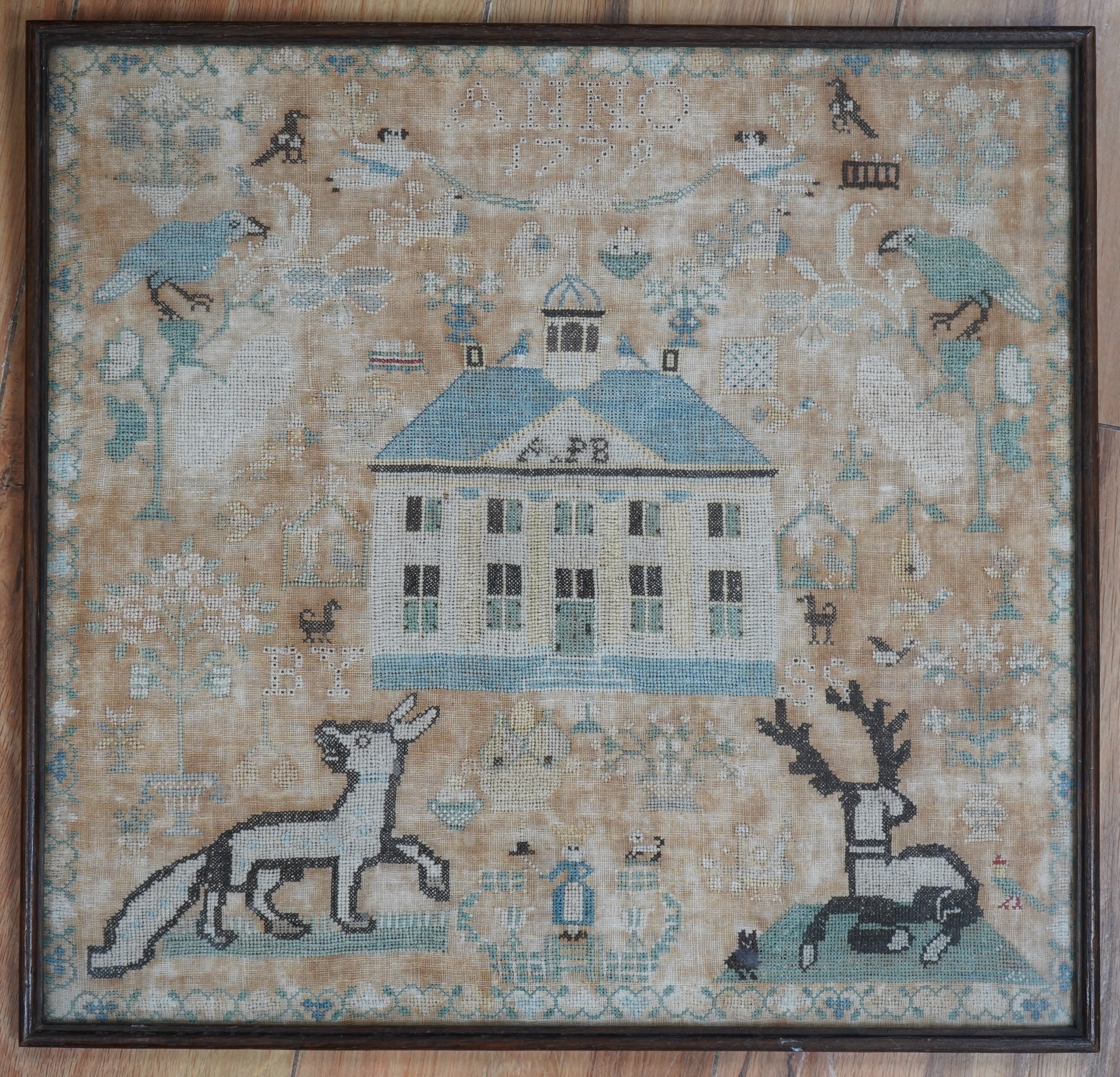 A framed 18th century sampler, dated 1779 by SS., worked in fine cross stitch with motifs of angels, figures, flowers, trees birds a fox and a stag surrounding a house with initials APB. 39cm x 37.5cm. Condition - the em